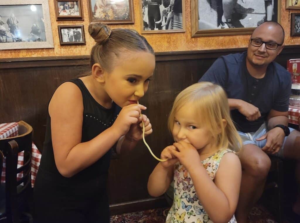 Two little kids sharing a noodle