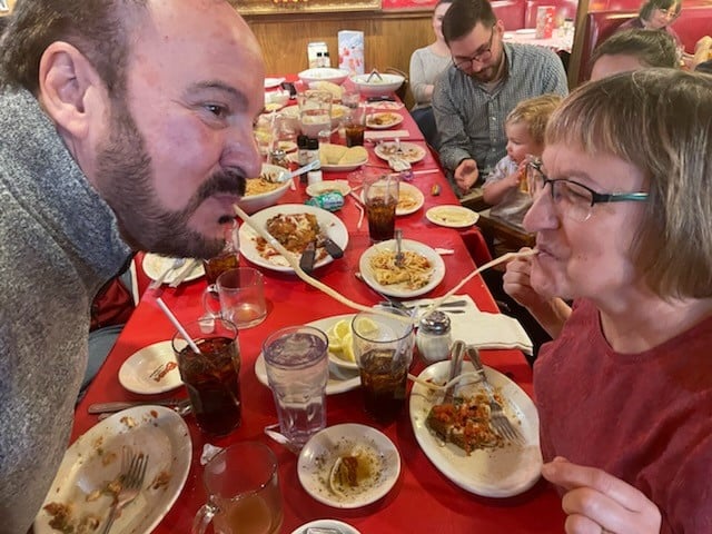 Two people sharing a noodle over a table full of food