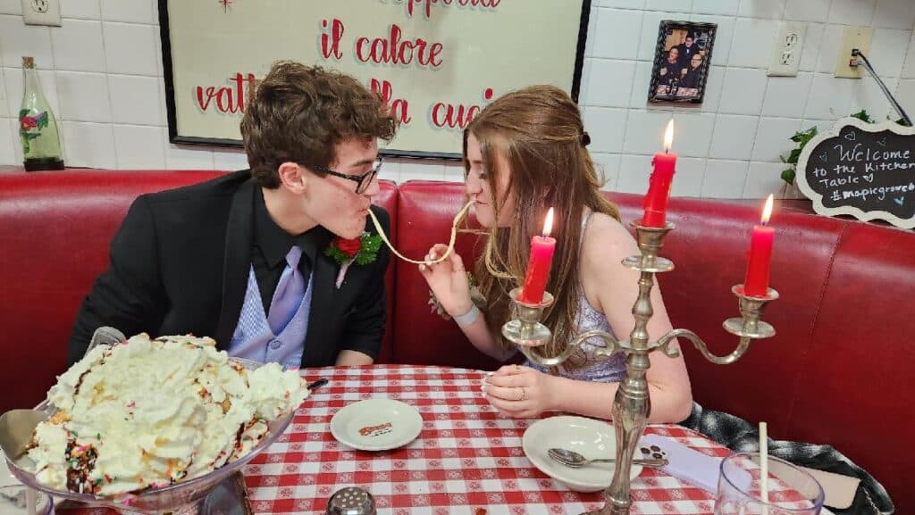 A couple in a booth seat sharing a noodle by candlelight
