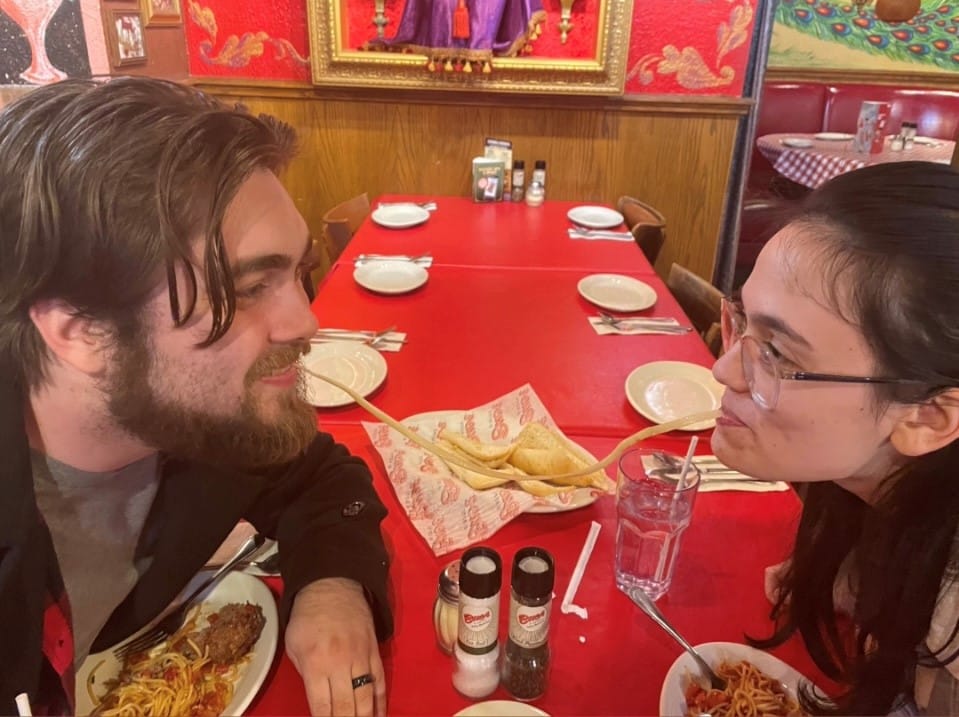A couple trying the pasta challenge and sharing a noodle across the table at Buca